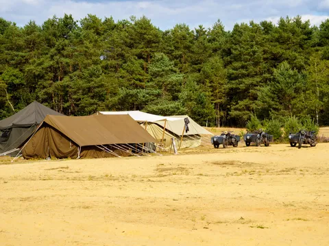 Military tents and vehicles pitched at the edge of a forest