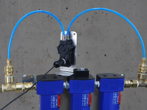 A differential pressure sensor piped across a row of compressed air filters on a wall