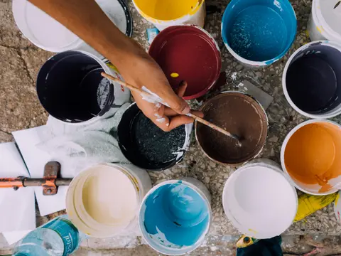 A hand mixing paint in open tins of colour
